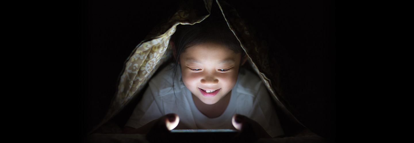 a child looking at their phone under a blanket
